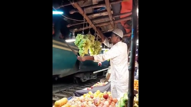 Sprzedawca owoców z Bangladeszu próbuje chronić swoje winogrona przed pasażerami pociągu