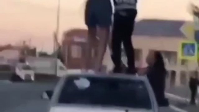 Dwoje ludzi stoi na dachu jadącego samochodu