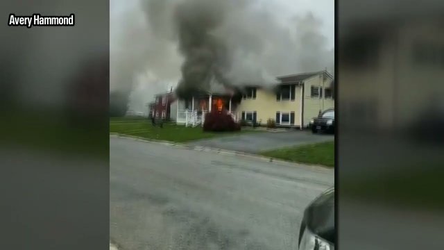 Kobieta podpala swój dom z osobą w środku i patrzy jak płonie siedząc na krześle ogrodowym