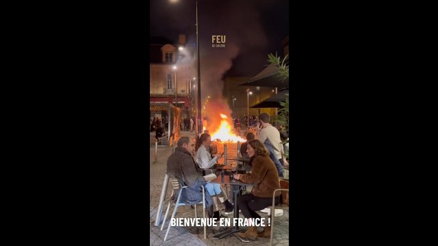 Francuzi spokojnie siedzą w kawiarni, podczas gdy w tle trwają protesty